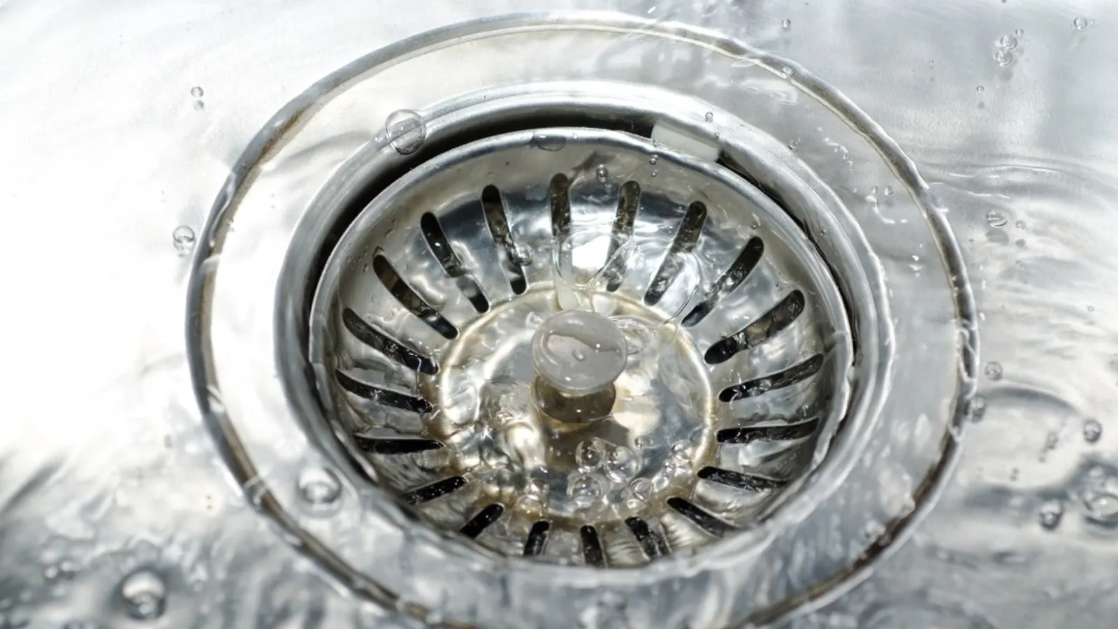 Water rippling over a stainless steel sink strainer basket as it drains