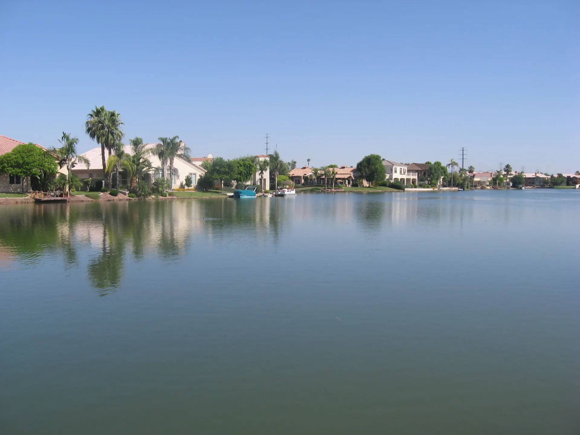 Calm lake water reflecting palm trees and homes along the lakefront at Val Vista Lakes in Gilbert, Arizona