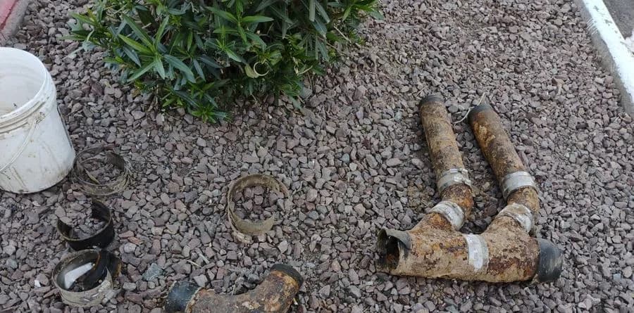 Sections of removed cast iron drain pipe on Arizona gravel, rust scaled and pitted, with the open bore ends visible