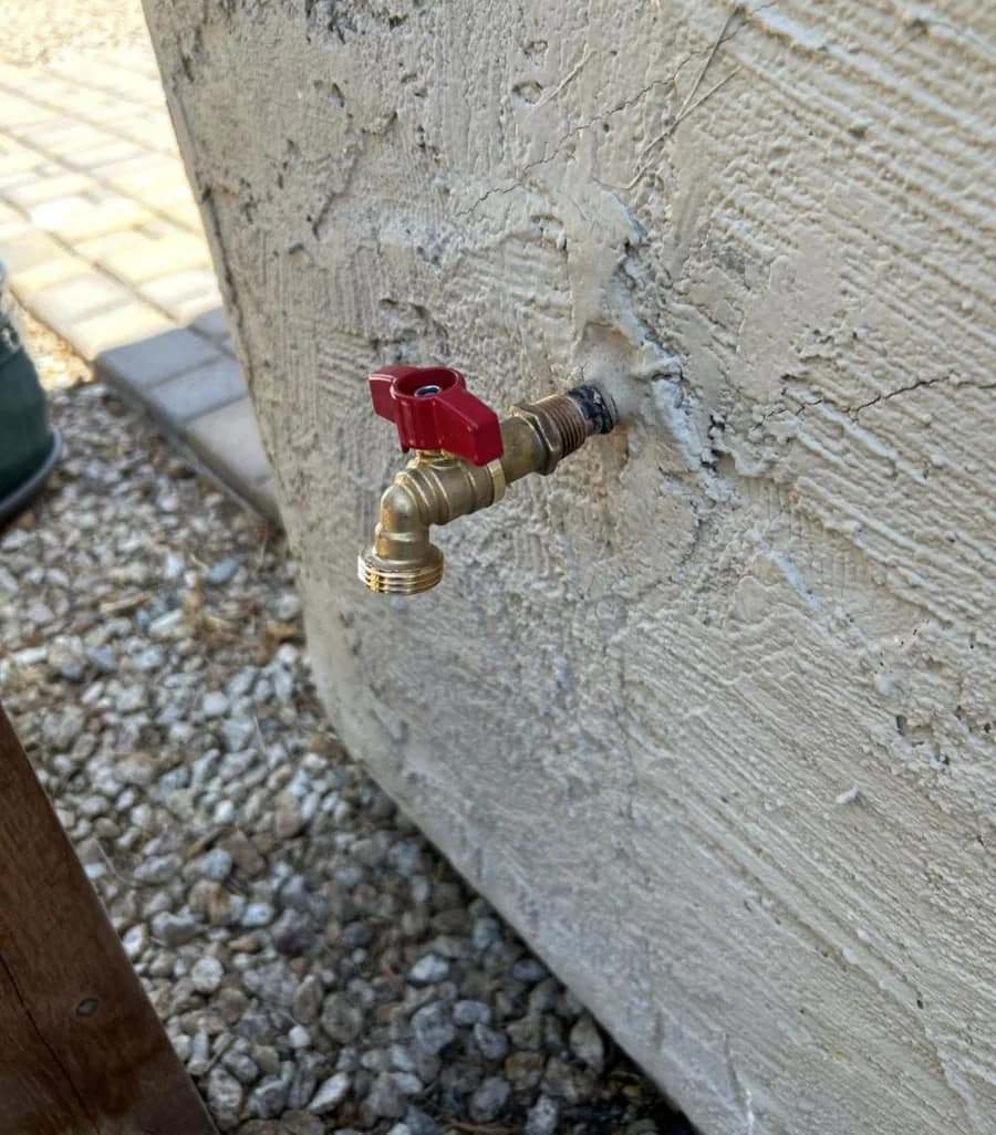 A new brass hose bib with a red lever handle installed into the stucco wall