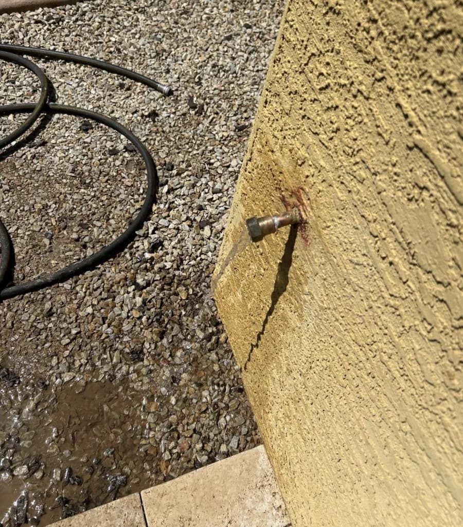 Water pooling in gravel below a leaking exterior hose bib at a stucco home
