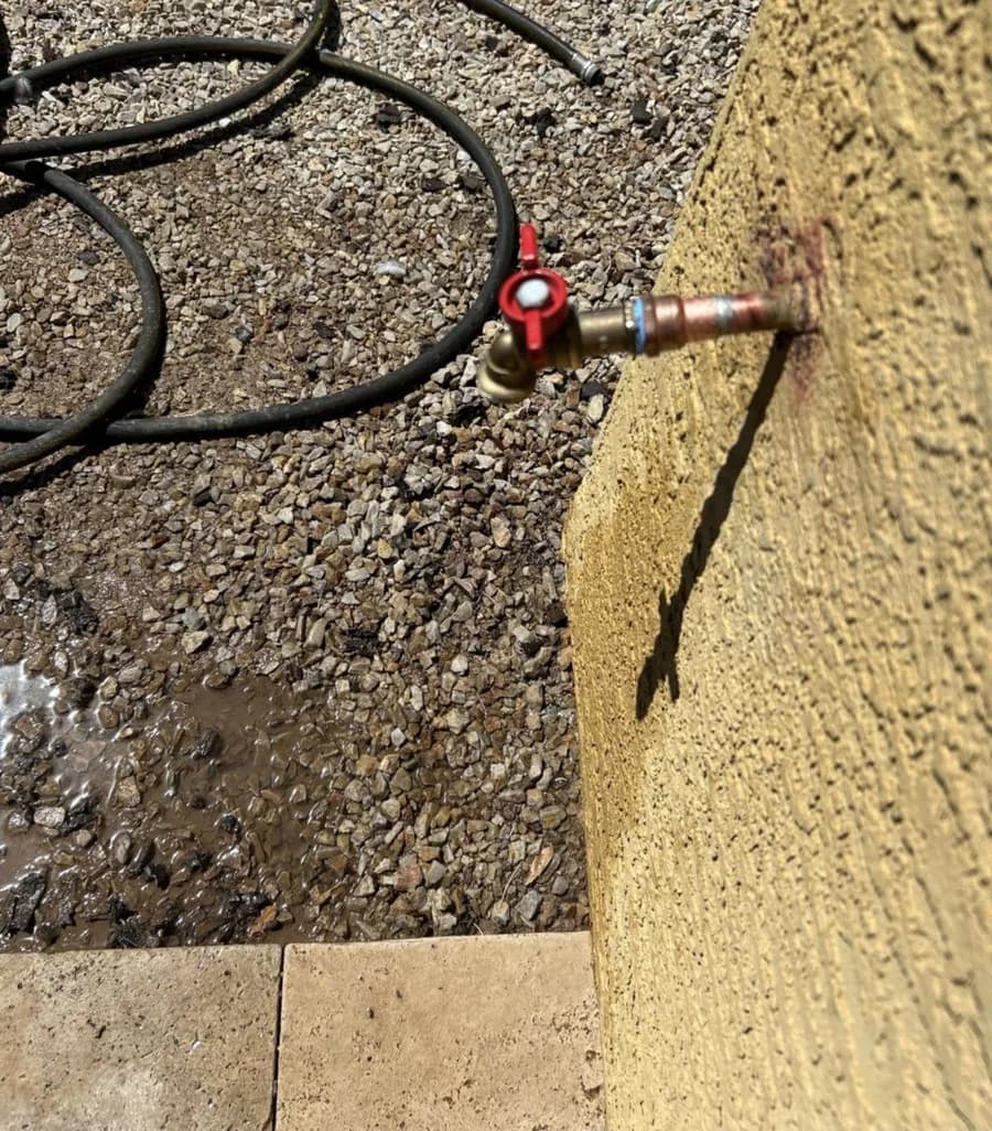A replacement brass ball-valve hose bib on a fresh copper nipple, with the wet gravel from the old leak still visible