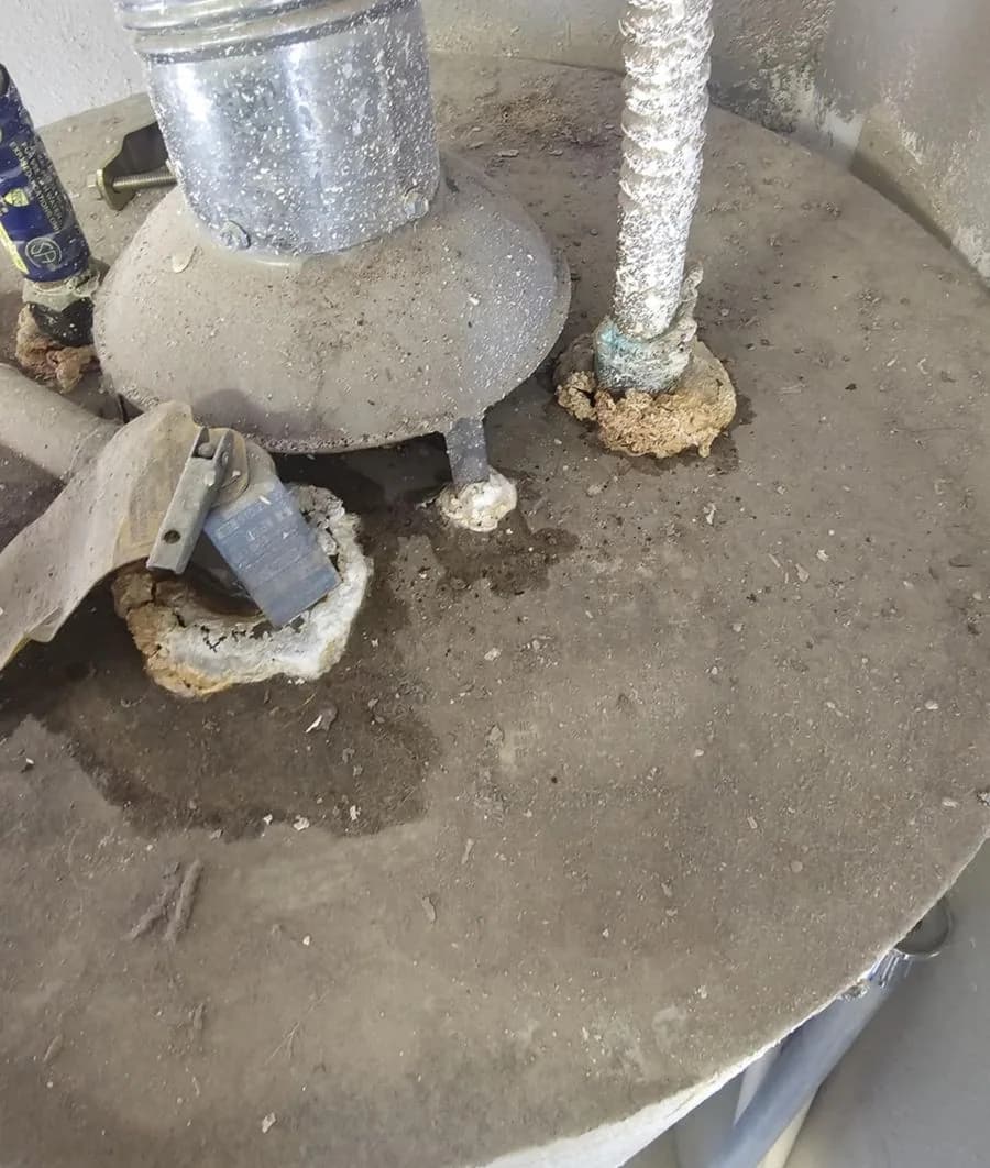Overhead view of a water heater showing mineral crust built up at both pipe penetrations around the draft hood