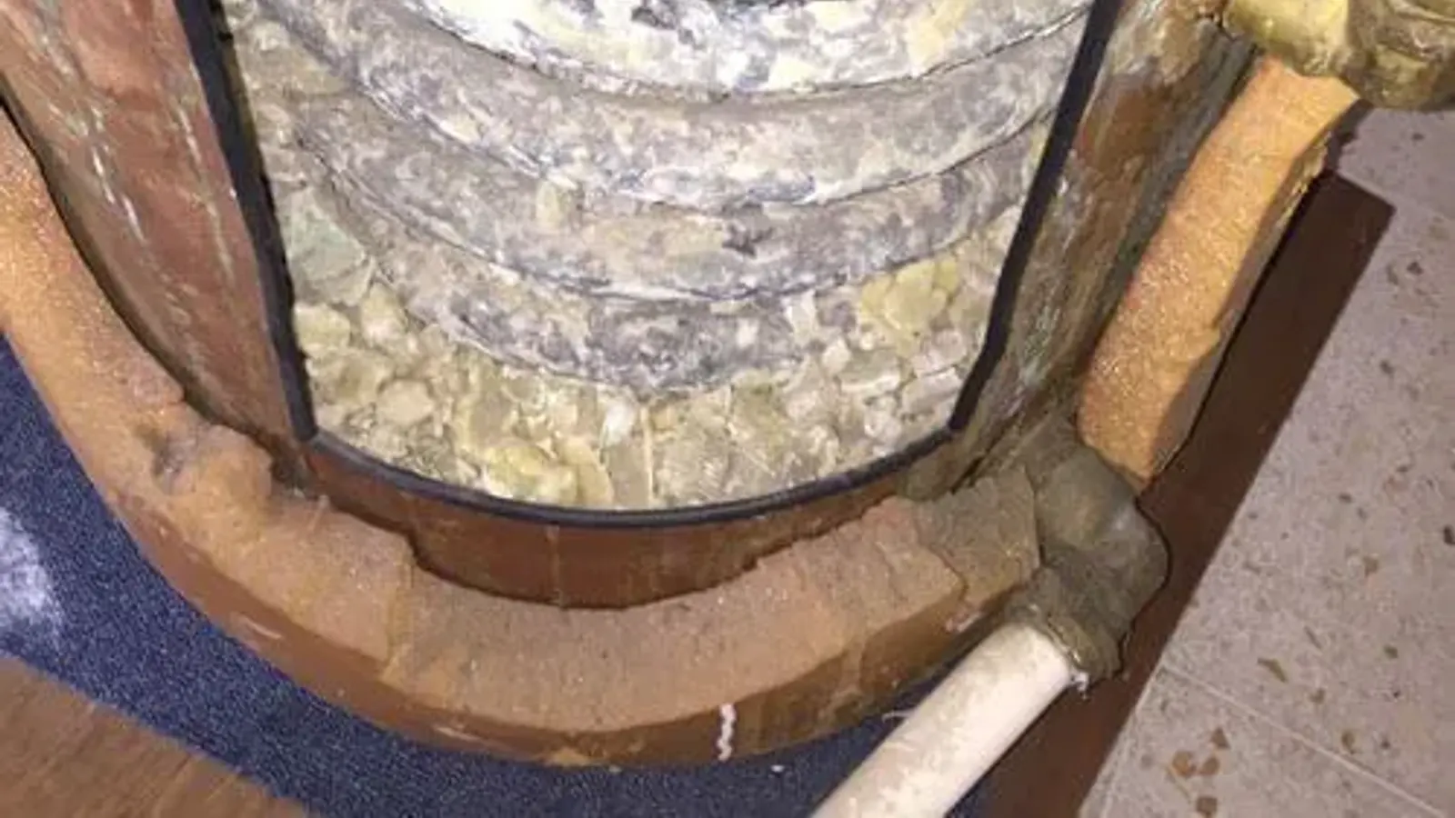 A cut-open water heater tank base, packed with crusty mineral sediment inside its foam-insulated shell