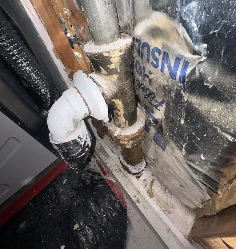 A vertical cast iron drain stack still in place inside an opened wall cavity